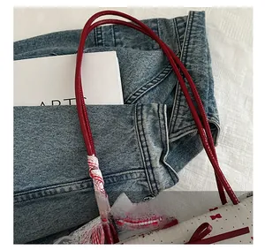Détail du sac blanc en toile à motifs de nœuds rouges et anses ornées de dentelle sur jean