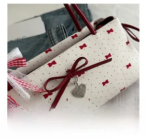 Détail du sac crème avec motifs de nœuds rouges, pois et pendentif en forme de cœur