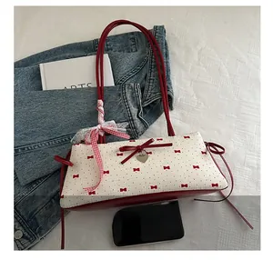 Détail du sac seau en tissu blanc avec motifs nœuds rouges et pendentif cœur en métal