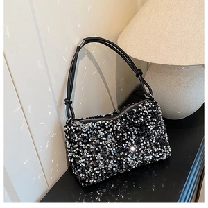 Detail of shimmering silver sequins on a black evening crossbody bag under warm light