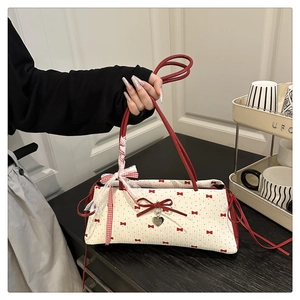 Détail du sac crème avec imprimés nœuds rouges et un pendentif en métal en forme de cœur