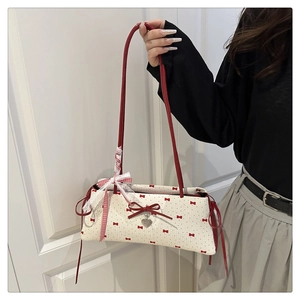 Détail du sac baguette blanc avec imprimés nœuds rouges et pendentif cœur en métal