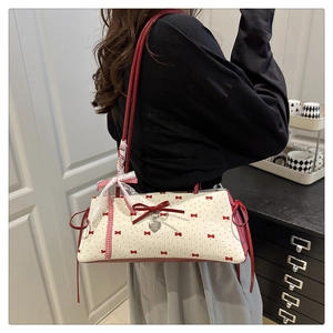 Détail du sac sous l'aisselle avec nœuds rouges et pendentif cœur sur tissu crème