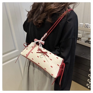 Détail d'un sac seau beige et rouge avec motifs de nœuds et breloque cœur sur un mannequin