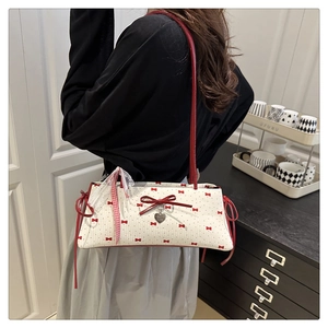 Sac bandoulière à nœuds rouges et pendentif cœur porté par un mannequin chez soi