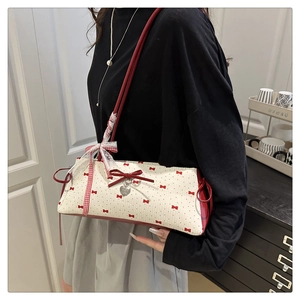 Détail du sac sous le bras en toile blanche avec nœuds rouges et pendentif cœur en métal