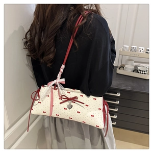 Détail du sac en tissu blanc avec imprimés nœuds rouges et un pendentif cœur en argent