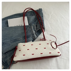 Détail du sac baguette blanc avec motifs de nœuds rouges et fines anses en cuir
