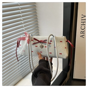 Détail du sac blanc avec nœud en cuir rouge, dentelle et breloque en forme de cœur