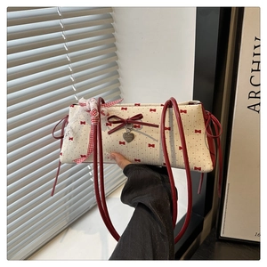 Détail du nœud rouge et du ruban de dentelle sur le sac baguette crème à motifs