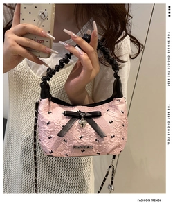 Detail of light pink pleated handbag with black silk bow and metal heart pendant accessory