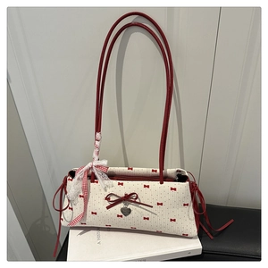 Détail du sac sous le bras beige avec nœud rouge, pendentif cœur et ruban dentelle