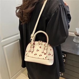 White cherry print semi-circle crossbody bag with adjustable strap worn by a model