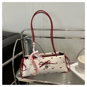 Détail du sac blanc à pois avec des nœuds rouges et un pendentif cœur argenté