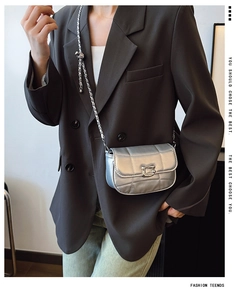 Détail du sac bandoulière argenté matelassé avec chaîne et boucle G sur un blazer gris