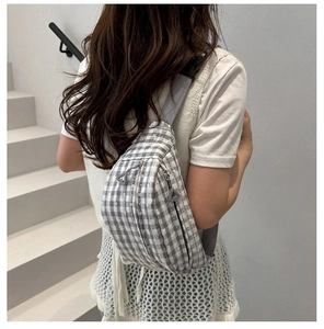 Detail of grey checkered crossbody bag with double zippers and fabric strap on model