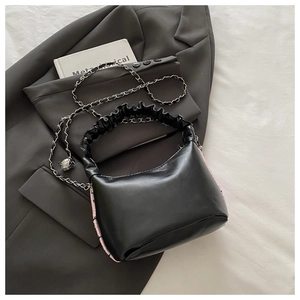 Detail of black leather handbag with silver chain strap and ruched handle on grey blazer
