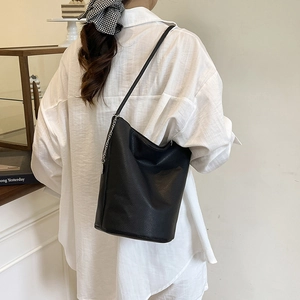 Minimalist black lychee leather bucket bag with silver chain worn by a woman in a cafe