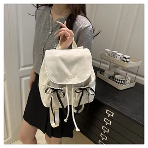 Détail d'un sac à dos beige avec broderie Nika et nœuds en ruban noir élégants