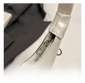 Close-up of polished silver-tone metal zipper and precise stitching on white leather bag