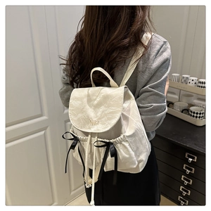 Détail du sac à dos crème avec nœuds en satin noir et broderie Nika sur tissu plissé