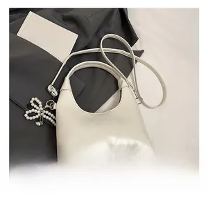 Detail view of white leather hobo bag featuring a decorative pearl bow charm accessory