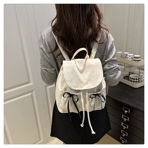 Détail d'un sac à dos blanc crème avec broderie Nika et nœuds décoratifs noirs