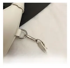 Detail shot of silver metal swivel hook and white leather strap on a shoulder bag