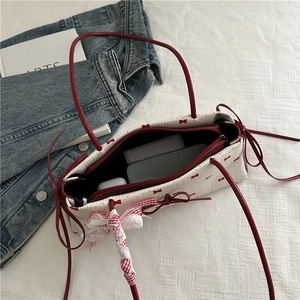Sac bandoulière blanc à nœuds rouges et dentelle, montrant la capacité pour objets du quotidien