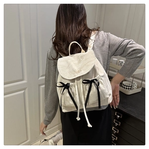 Close-up of white ruffled backpack with Nika embroidery and black ribbon bow details