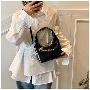 Detail of black crescent moon patent leather handbag with pearl bow pendant and shoulder strap