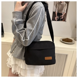 Vue latérale du sac bandoulière en nylon noir imperméable avec étiquette en cuir sur modèle