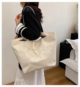 Detail of beige canvas tote bag with letter print shown worn on model's shoulder
