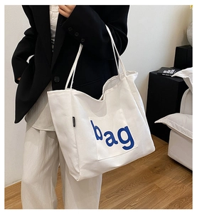 Detail of white canvas tote bag featuring blue bag lettering and fashion side label