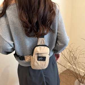 Sac de poitrine minimaliste en nylon beige avec bandoulière noire sur un modèle féminin