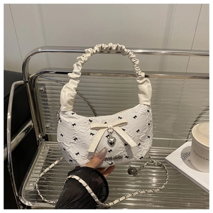 Detailed view of white pleated handbag with black bow patterns and heart pendant