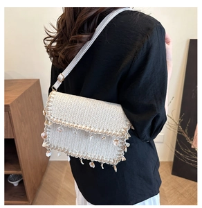 Detail of straw woven crossbody bag with hanging sea shells and white shoulder strap
