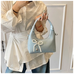 Detail of light blue patent leather hobo bag with pearl bow and silver heart pendant