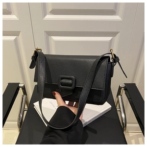 Close-up of black litchi grain leather shoulder bag with gold metal buckle and flap