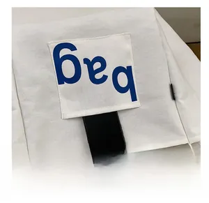 Detail of the white canvas tote bag side pocket with blue 'bag' lettering