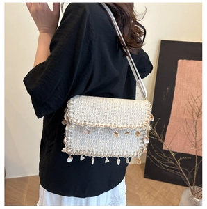 Detail of bohemian woven beige straw shoulder bag with shell charms on a model