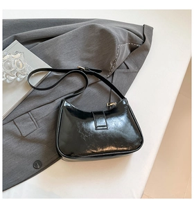 Dettaglio borsa hobo in pelle verniciata nera con cerniera dorata su sfondo minimalista