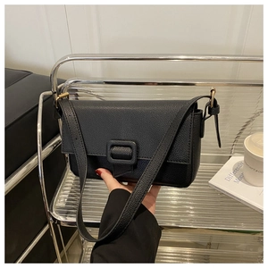 Close-up of black litchi pattern leather shoulder bag with gold hardware on a metal shelf