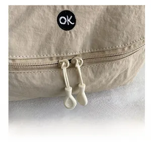 Detail of beige nylon bag showing smooth dual-zipper closure and 'ok' embroidery