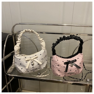 Detail of ruched shoulder bag featuring bow embroidery and heart pendant on metal shelf