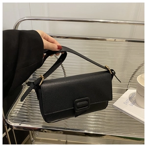 Detail of black lychee-grain leather baguette bag featuring golden hardware and a square buckle