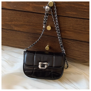 Gros plan sur la texture en cuir matelassé noir et la chaîne argentée du sac chic