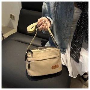 Gros plan sur un sac bandoulière en nylon kaki clair avec étiquette cuir et fermetures éclair