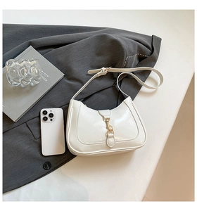 Borsa a mezzaluna in pelle lucida bianca con chiusura a pistone oro su abito grigio