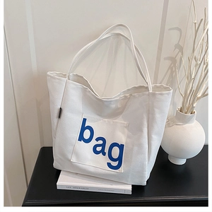 Detail of canvas tote bag with front pocket featuring blue bag text and long straps